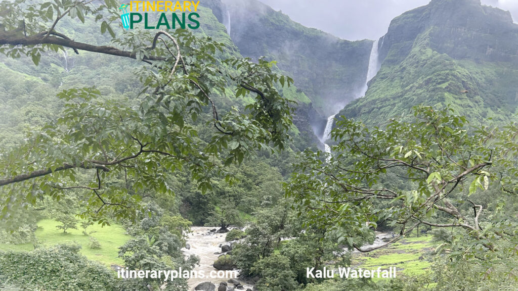 Lush green landscape with a cascading waterfall in the distance, framed by leafy trees. A flowing river in the foreground adds to the serene atmosphere.