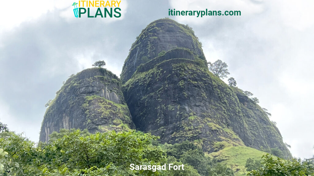 Sarasgad Fort set against a cloudy sky, with rugged green and black cliffs partially covered in trees, evoking a serene, majestic feel.