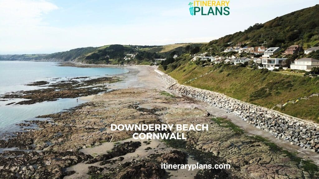 Scenic view of Downderry Beach Cornwall with rocky shoreline, calm sea, and hillside houses under a clear blue sky.