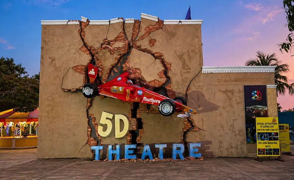 A red Formula 1 car appears to crash through a cracked wall labeled "5D Theatre" at sunset. The vibrant and dynamic scene suggests excitement.