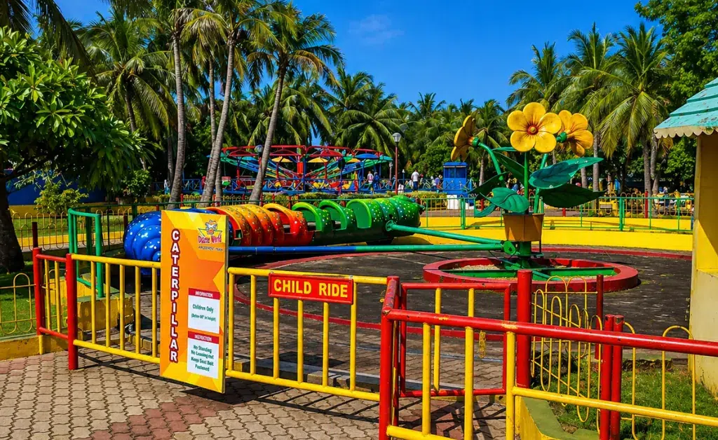 A colorful children's caterpillar ride in a tropical park, surrounded by lush palm trees. The setting feels vibrant and inviting on a sunny day.