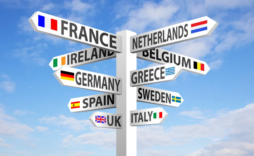 A signpost with directional arrows shows names and flags of France, Netherlands, Ireland, Belgium, Germany, Greece, Sweden, Spain, UK, and Italy against a blue sky.