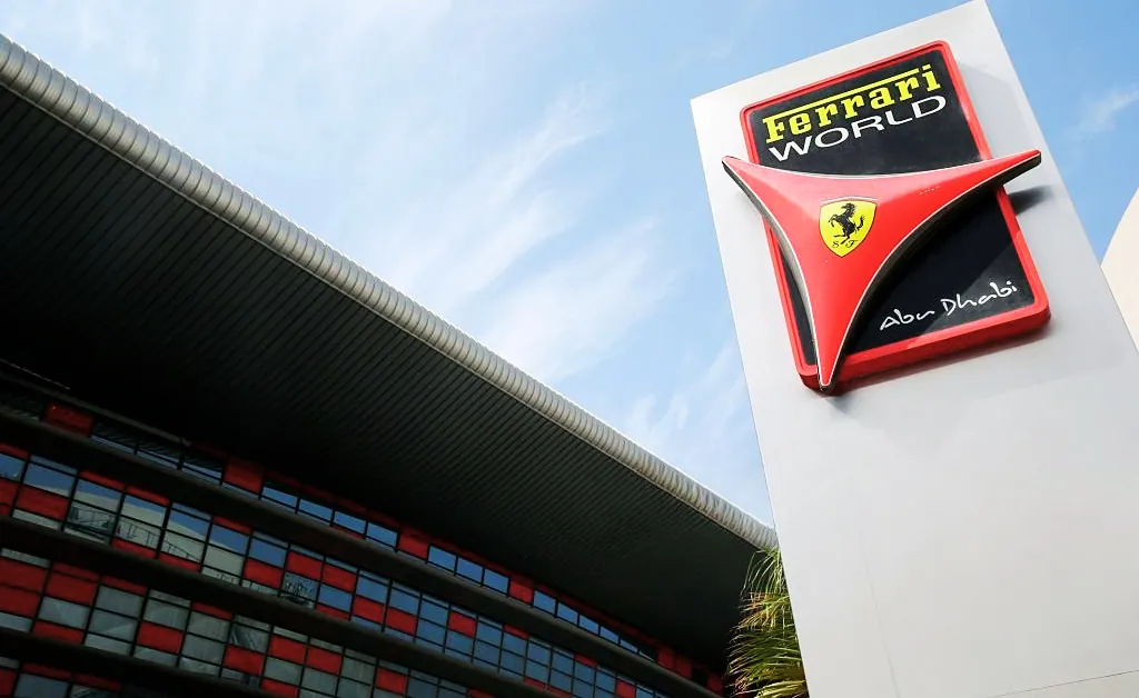 Ferrari World Abu Dhabi entrance with a large sign featuring the Ferrari logo. The building has a sleek, modern design with red and black accents against a blue sky