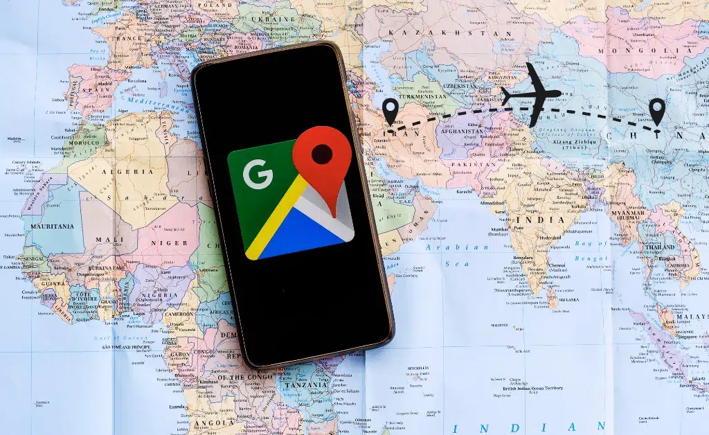 A smartphone displaying the Google Maps logo rests on a world map, illustrating digital navigation. An airplane icon connects location pins, symbolizing travel.