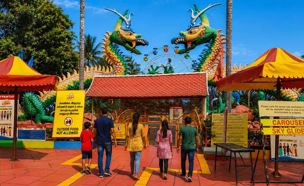 A group of people walk toward a colorful amusement park entrance with large dragon statues. Signs read "Outside Food Not Allowed." The sky is clear.