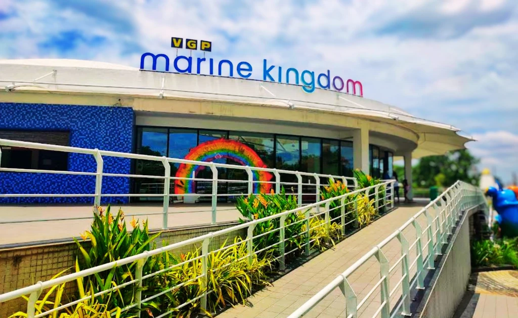 Entrance of VGP Marine Kingdom showing a vibrant rainbow mural, clear sky, ramp, plants, and inviting atmosphere, suggesting a family-friendly venue.