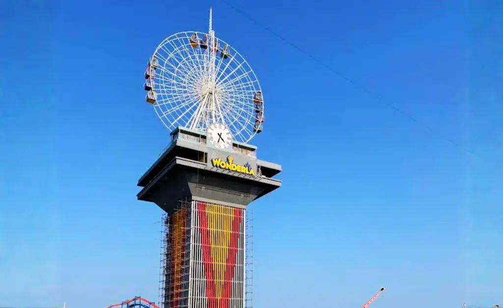 A tall amusement park tower with a large Ferris wheel on top, set against a clear blue sky. The structure has a "Wonderla" logo and colorful vertical accents.