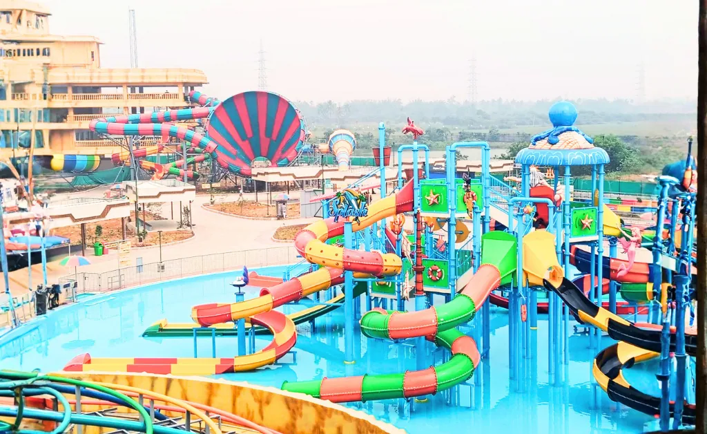 Bright, colorful water park filled with winding slides, splash zones, and pools. The scene conveys excitement and fun under a clear sky.