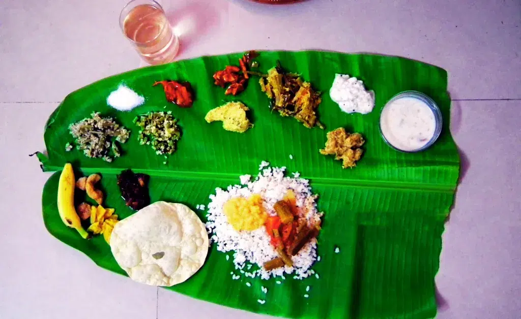 A traditional South Indian meal on a banana leaf with rice, various curries, fried snacks, and a glass of water, conveying a vibrant and cultural feast.