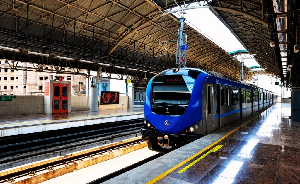 Blue metro train at a modern, covered station, arriving on shiny tracks under an arched roof, conveying a sense of efficiency and urban transit.
