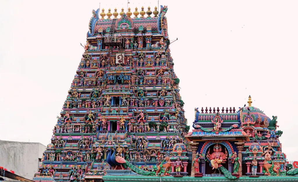 A vibrant, intricately decorated Hindu temple gopuram adorned with colorful statues and carvings against a light sky, conveying a sense of cultural richness.